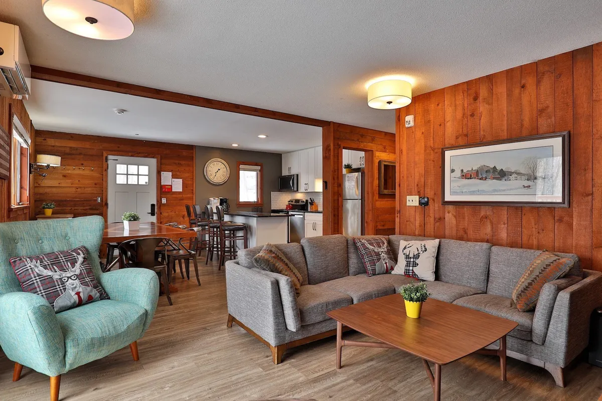 An open-concept living, dining, and kitchen area, featuring a comfortable sofa, inviting blue armchair, a dining table ready for group meals, and a kitchen visible in the background. The layout encourages interaction and shared experiences.