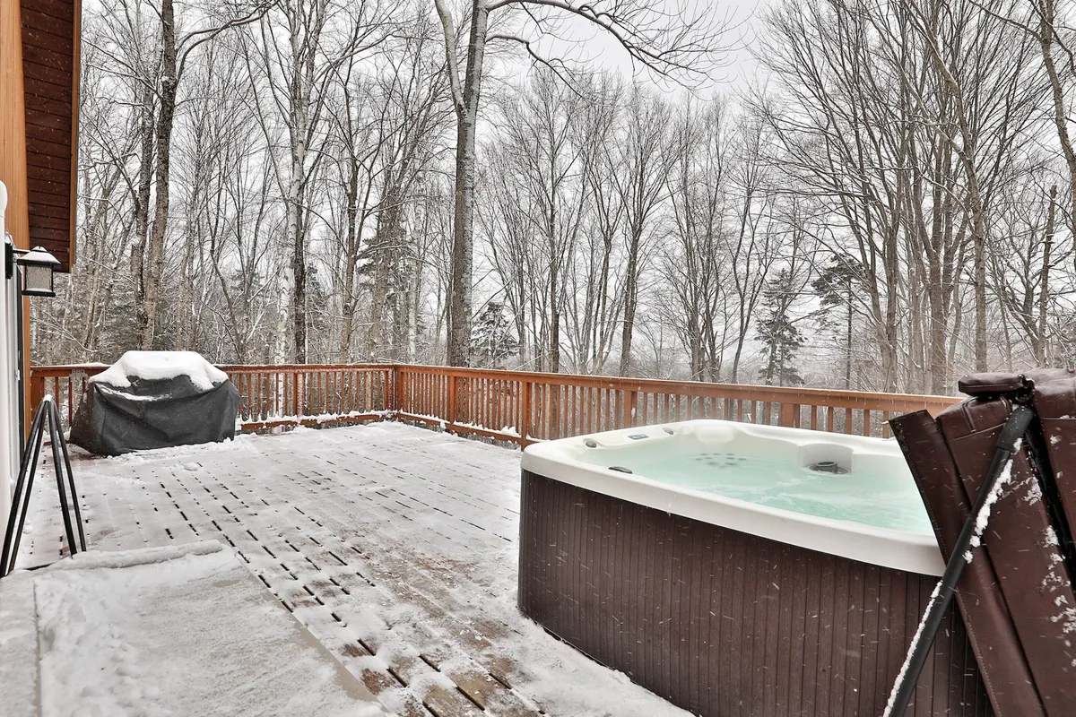 An inviting hot tub set on a wooden deck, surrounded by snow-covered trees, offering a serene outdoor relaxation experience even in winter.
