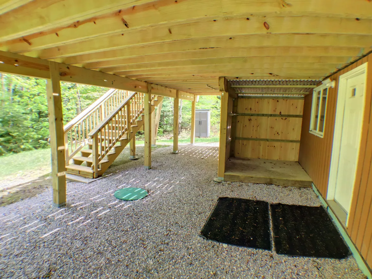 A casual outdoor area with a sturdy wooden staircase, gravel flooring, and covered storage. The space is informal and functional, offering shelter and flexible gathering spots for groups to socialize or prep for an outing.