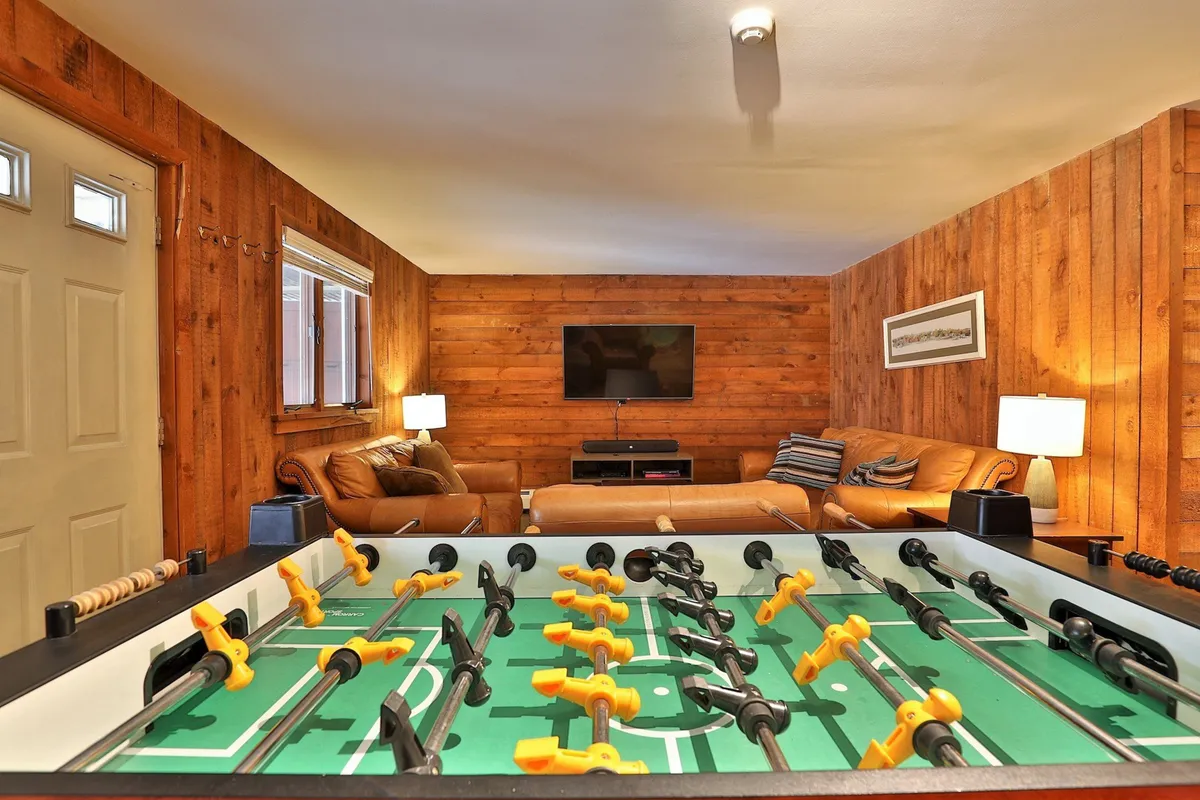 A cozy game room featuring a foosball table, leather sofas, a television, and warm wood paneling. The playful, communal atmosphere is ideal for friendly competition and shared laughter among family and friends.