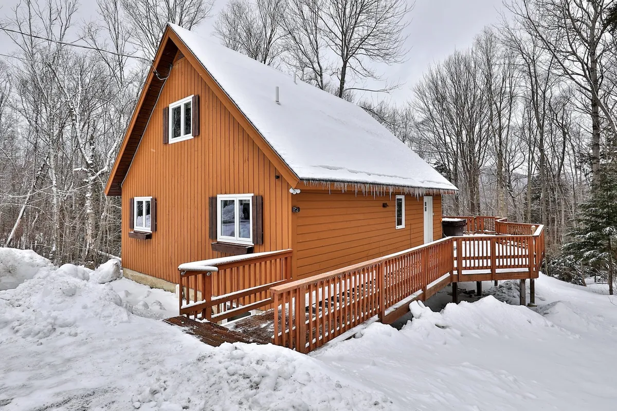 This image showcases the home's wooden deck and orange exterior, set against a snow-covered roof and wintry landscape. The outdoor space is inviting, with ample room for gatherings and activities, and highlights the connection between the house and its natural Vermont surroundings.
