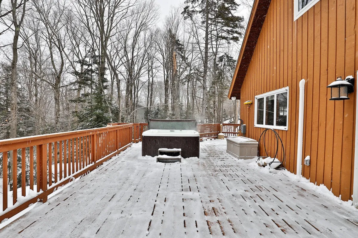 The image displays a hot tub set on a wooden deck surrounded by trees, with a peaceful atmosphere ideal for relaxation. The setting is perfect for showcasing the seasonal amenity of the hot tub, which is mentioned as a flexible comfort that adapts to guest needs.