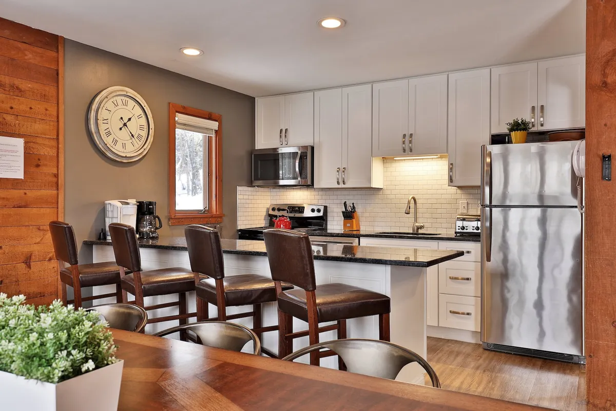 A welcoming, newly remodeled kitchen with a spacious island counter, bar stools, modern appliances, and a wall clock. The space is bright and open, inviting guests to gather, cook, and socialize.