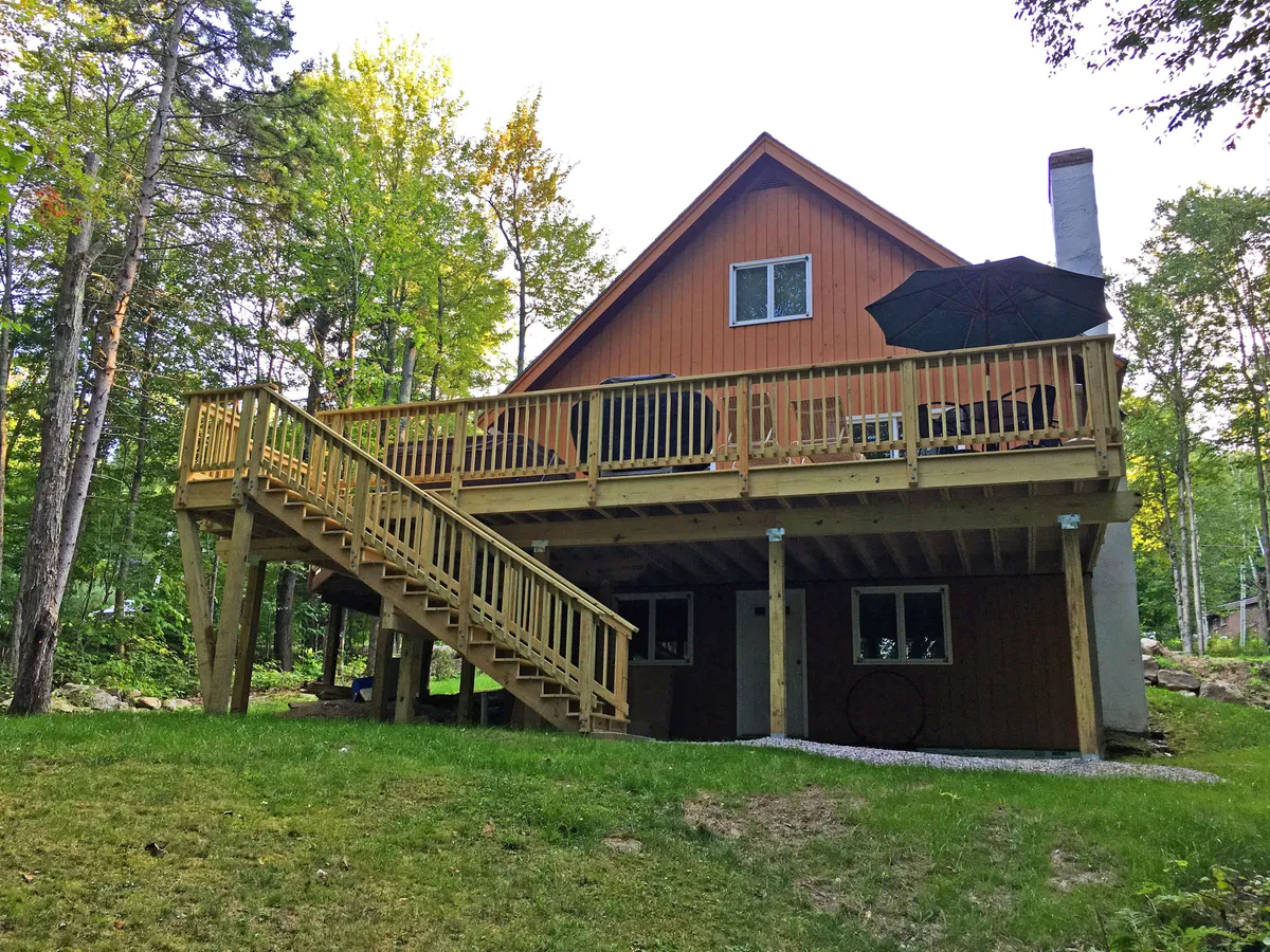 A cozy wooden outdoor deck with a staircase, surrounded by green trees and featuring an umbrella for outdoor dining. The space is inviting for morning coffee, sunset gatherings, or simply enjoying mountain views.